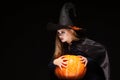 Halloween Witch with Pumpkin on black background. Beautiful young surprised woman in witches hat and costume holding Royalty Free Stock Photo