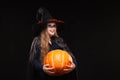 Halloween Witch with Pumpkin on black background. Beautiful young surprised woman in witches hat and costume holding Royalty Free Stock Photo