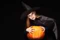 Halloween Witch with Pumpkin on black background. Beautiful young surprised woman in witches hat and costume holding Royalty Free Stock Photo