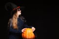 Halloween Witch with Pumpkin on black background. Beautiful young surprised woman in witches hat and costume holding Royalty Free Stock Photo