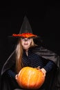 Halloween Witch with Pumpkin on black background. Beautiful young surprised woman in witches hat and costume holding Royalty Free Stock Photo