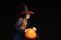 Halloween Witch with Pumpkin on black background. Beautiful young surprised woman in witches hat and costume holding Royalty Free Stock Photo