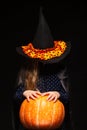 Halloween Witch with Pumpkin on black background. Beautiful young surprised woman in witches hat and costume holding Royalty Free Stock Photo