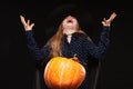 Halloween Witch with Pumpkin on black background laughs evilly. Beautiful young surprised woman in witches hat and Royalty Free Stock Photo