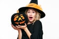 Halloween Witch with shocked expression holding a Jack o Lantern. Beautiful young woman in witches hat and costume holding pumpkin Royalty Free Stock Photo