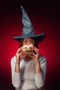 Halloween. A young woman in a black witch hat is holding a pumpkin with a zombie face. Vertical Royalty Free Stock Photo