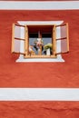 Hallstatt, Austria, 27 August 2021: open wooden window with vase of flowers and statue of orange cat, red and white wall, exterior