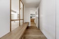 Hallway of a home with white wooden built-in wardrobes, a long wooden bench next to a skylight with a wooden structure and