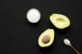 Halved avocado and sea salt over black surface, top view. Flat lay, overhead, from above Royalty Free Stock Photo