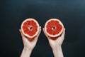 Hands holding halved grapefruit on a black background with water drops. Royalty Free Stock Photo