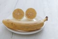 Halved lemon and banana on a white plate on a background of a gray wooden table. Royalty Free Stock Photo