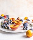 Halved peaches, nectarines, grapes, figs on white plate, cutlery on white tablecloth, front view
