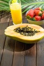 Halved Ripe Papaya Fresh Strawberries in Bowl Pineapple Juice in Tall Glass with Straw Palm Leaf on Plank Wood Table