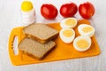 Halves of boiled eggs, bread on cutting board, salt shaker, tomatoes on wooden table Royalty Free Stock Photo