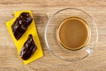 Pieces of eclairs with chocolate on paper napkin, cup of coffee with milk on saucer on table. Top view Royalty Free Stock Photo