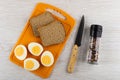 Halves of boiled eggs, bread on cutting board, knife, jar with condiment on wooden table. Top view Royalty Free Stock Photo