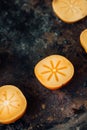 Halves of persimmon fruit on black metal surface.