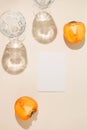 Halves of persimmon fruit with paper card note and two glasse with water on beige pastel background. Summer refreshment