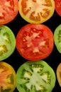 Halves of red, green and yellow tomatoes on black background top view Royalty Free Stock Photo