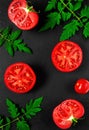 Halves of ripe red tomatoes, leaves and branches of tomatoes on a black stone background. Ripe vegetables, ingredients for the