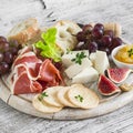 Ham, cheese, grapes, figs, nuts, bread ciabatta, cracker, jam on white wooden board on bright wooden surface. Rustic style. Royalty Free Stock Photo