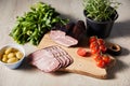 Ham on cutting board with greens, cherry tomatoes, olives on wooden table