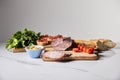 Ham on cutting board with parsley, cherry tomatoes, olives and baguette on white marble surface isolated on grey