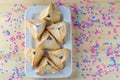 Hamantaschen cookies on white dish on wood desk colorful confetti background. Purim holiday celebration.Top view.