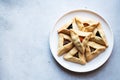 Hamantashen with diferent fillings on a white plate on a gray background. It is traditional bakinf for Purim, Jewish holiday