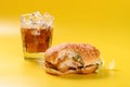 Hamburger with a bite and cup of iced cola on yellow background