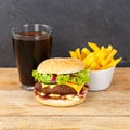 Hamburger Cheeseburger meal fastfood fast food with cola drink and French Fries on a wooden board square Royalty Free Stock Photo
