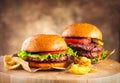 Hamburger and Double Cheeseburger with fries rotated on wooden table background. Cheeseburgers on fresh buns with succulent beef Royalty Free Stock Photo