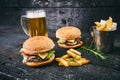 Hamburger with french fries, beer on a burnt, black wooden table. Fast food meal. Homemade hamburger consist of beef meat, lettuce