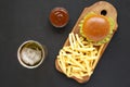 Hamburger, french fries, sauce and glass of cold beer on a black surface, top view. Flat lay, from above, overhead Royalty Free Stock Photo