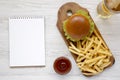 Hamburger, french fries, sauce, glass of cold beer and blank notepad on a white wooden background, top view Royalty Free Stock Photo