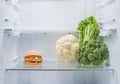 Hamburger and fresh vegetables opposite each other in an empty refrigerator.
