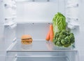 Hamburger and fresh vegetables opposite each other in an empty refrigerator.