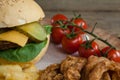 Hamburger, onion ring, cherry tomato and french fries on chopping board