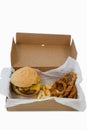 Hamburger, onion ring and french fries in a take away container on table