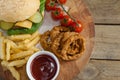 Hamburger, onion ring, tomato sauce, cherry tomato and french fries on chopping board