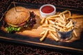 Hamburger with sauce and a bucket of french fries on a wooden plate Royalty Free Stock Photo