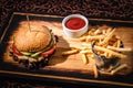 Hamburger with sauce and a bucket of french fries on a wooden plate Royalty Free Stock Photo