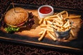 Hamburger with sauce and a bucket of french fries on a wooden plate Royalty Free Stock Photo