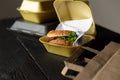 Hamburger in a takeaway container on the wooden background. Food delivery and fast food concept