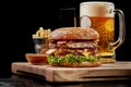 Hamburger with two patties, bacon, cheese, caramelized onions, tomatoes served with light beer, fries and aioli Royalty Free Stock Photo