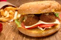 Hamburger on the wooden table with french fries. Delicious lunch with cheese, tomatoos and salad