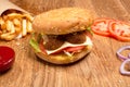 Hamburger on the wooden table with french fries. Delicious lunch with cheese, tomatoos and salad