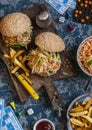 Hamburgers with grilled chicken and cole slaw on a wooden board on the table with cards and bingo chips, top view.