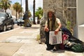 Hamilton, Bermuda - July 10, 2014: An old homeless black man with dreadlocks sitting on the street with a newspaper in his hand.