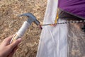 Hammer putting a nail-like tent peg out of iron into the grass on the ground. Push the anchor of the tent onto the ground.Travel